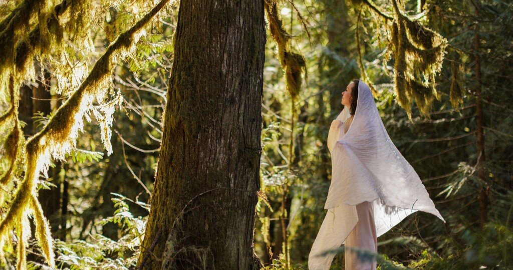 Angela Bolton in a white veil, looking up through moss-hung cedars