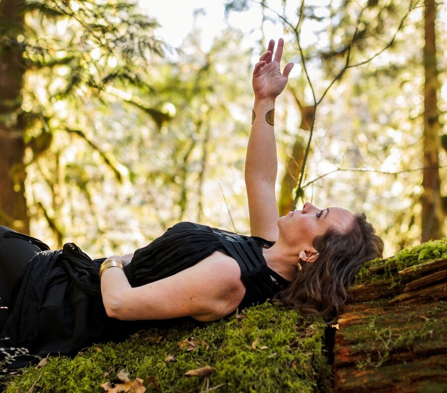 Angela Bolton lying on a moss-covered log, one hand raised to the light