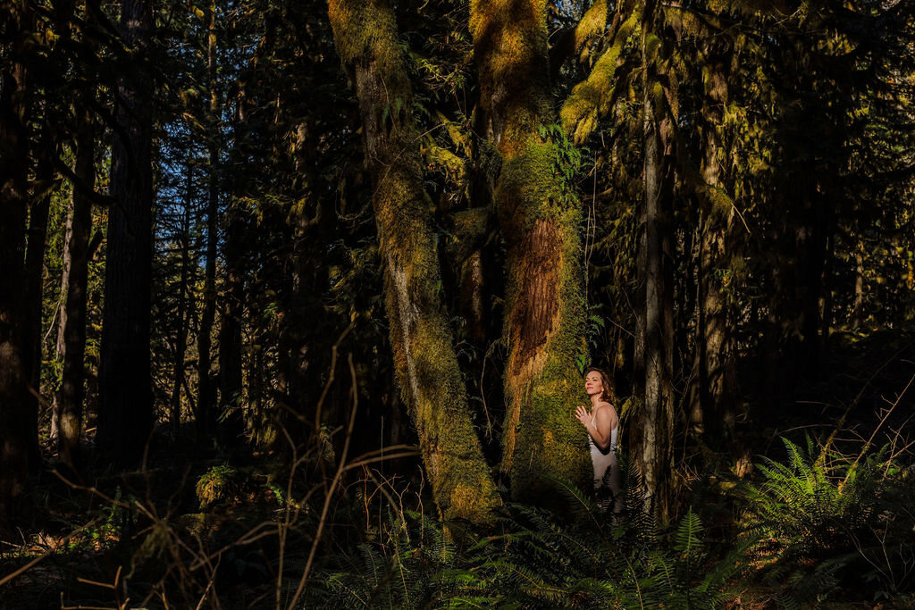 Angela Bolton small and pale-robed at the foot of an immense moss-hung tree in deep forest