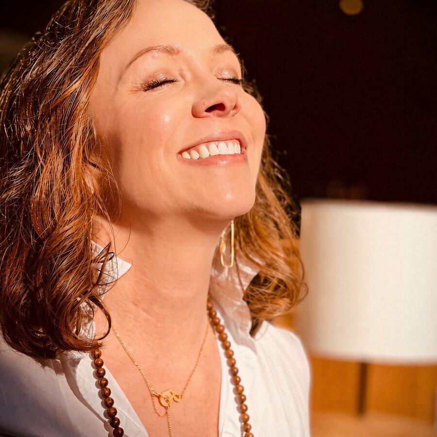 Angela Bolton laughing with her head tipped back, a warm lamp blurred behind her