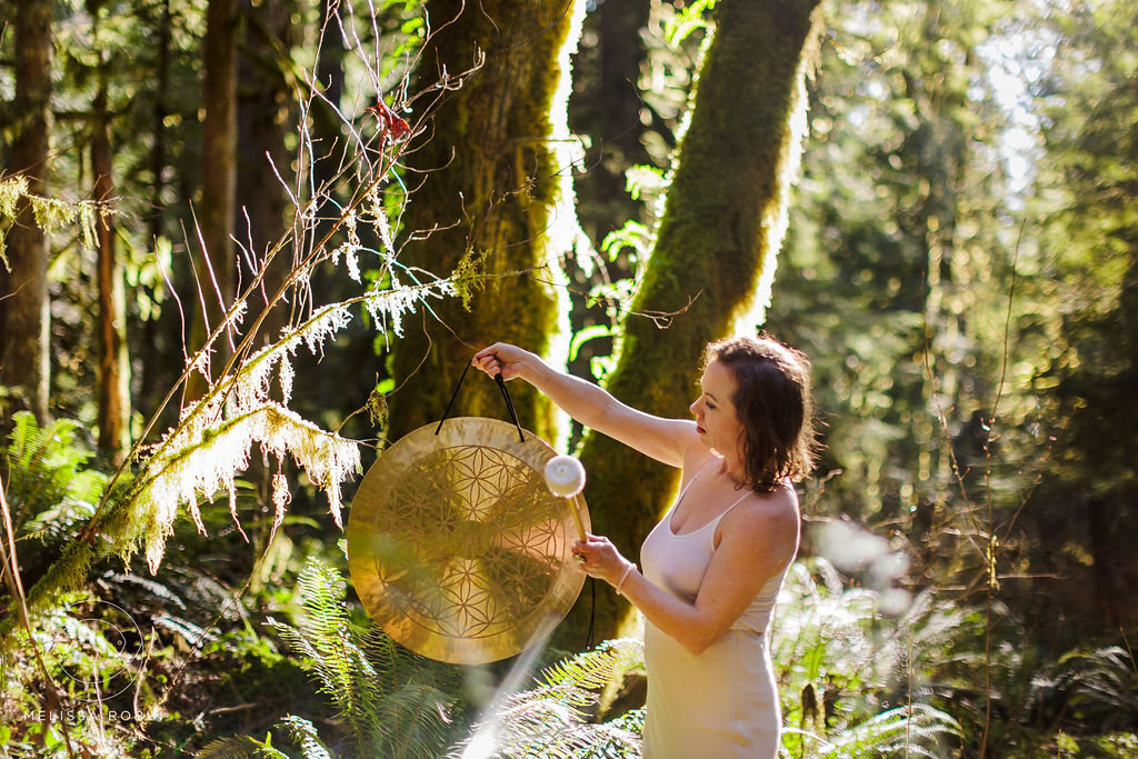Angela Bolton holding a Flower of Life gong in a sunlit forest