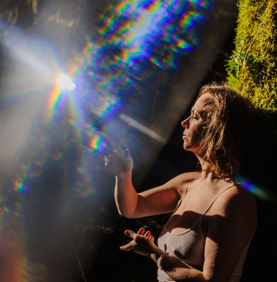Angela Bolton in profile with her eyes closed and hands open, a burst of prismatic light across the frame