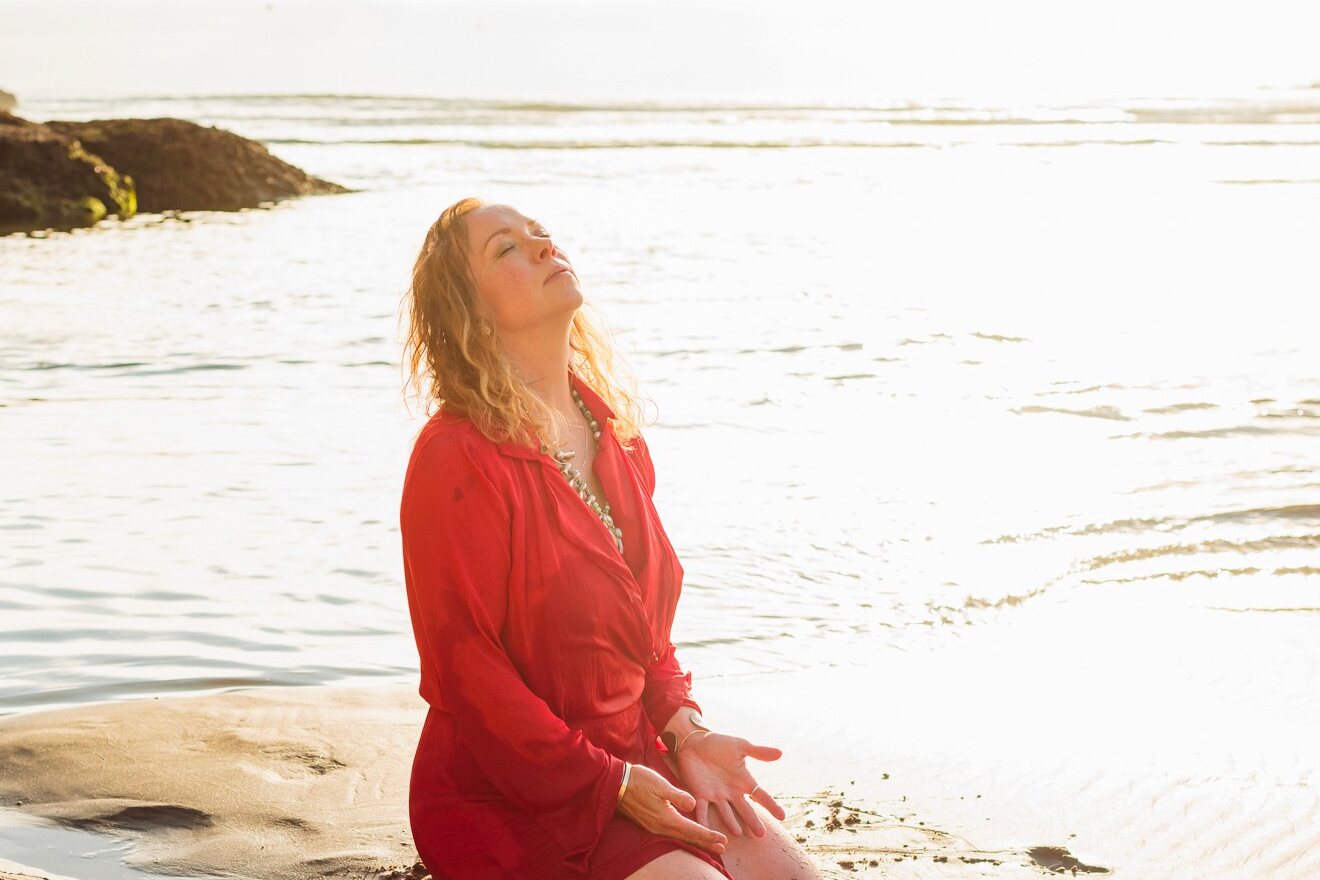 Angela Bolton kneeling at the tide line at sunrise, head tipped back