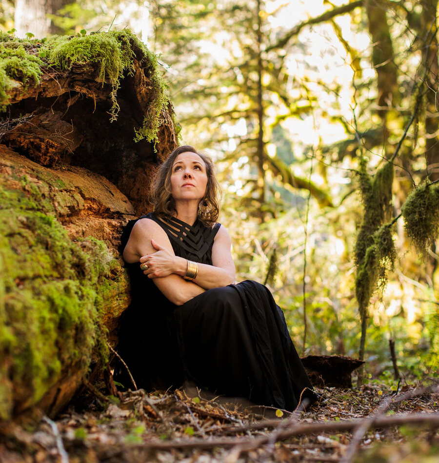 Angela Bolton sitting in the hollow of a moss-covered fallen tree, looking up into the canopy